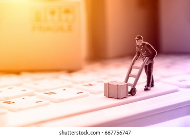 Miniature messenger in a blue dress with a crate or wooden box on a white keyboard. Concept of delivery parcel to customers who ordered / bought things or goods from online stores by using internet.