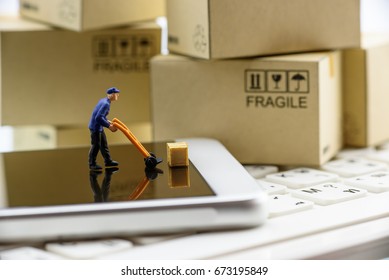 Miniature messenger with a wood crate on a white smart phone with paper boxes behind. Concept of shipment, customers always order things from online stores and the messenger will pick up and send it.