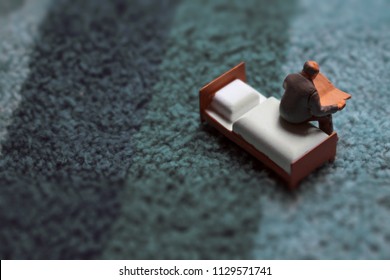 Miniature Middle Aged Or Elderly Man Reads On A Tiny Bed.  Man In His Home With Vintage Shag Rug Texture. Sitting Down With A Good Novel, Newspaper, Or Magazine.