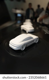 A miniature model of a Porsche car. White car models are displayed as exhibits that people look at. A prototype car. Car model.