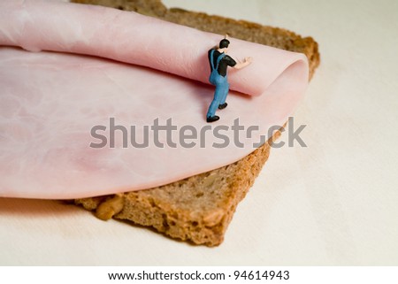 A miniature model workman rolls out a slice of ham on a slice of brown bread, back view with copyspace.