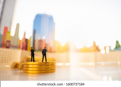 Miniature People: Business Man Standing On Stack Of Gold Coins On Blurred City Scape With Copy Space Using As Background Business Investment, Bank Financial Concept.