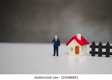 Miniature People, Businessman Standing With Mini House Using As Business And Family Concept