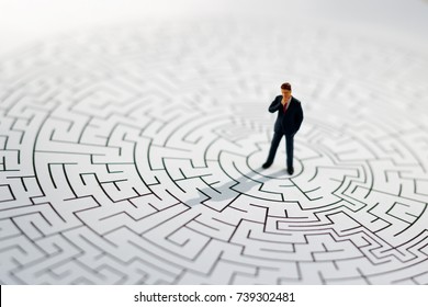 Miniature people: Businessman standing on center of maze. Concepts of finding a solution, problem solving and challenge.