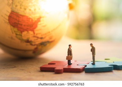 Miniature People : Businessmen Making A Deal On The Colorful Jigsaw Puzzle With World Map As Background. Business Concept, Agreement, Achievement, And Success.