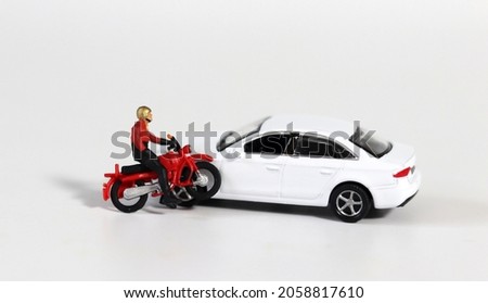 Miniature people and miniature car. A miniature motorcycle rider in front of a white miniature car. Concept about a dangerous motorcycle accident.
