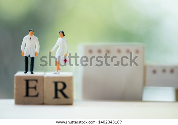 Miniature people:\
Doctor and nurse standing on wooden block with words ER. Health\
care and emergency\
concept.