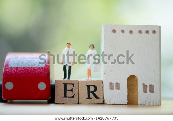 Miniature people: Doctor and nurse standing on\
wooden block with words ER, car and hospital. Concept of prepared\
emergency in long\
holiday