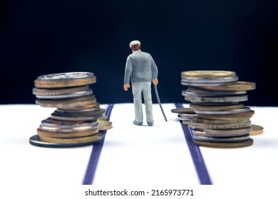 Miniature People. An Elderly Pensioner With A Stick Against The Background Of Money Walks The Road Until The End Of His Life. Pension And Financial Security For The Elderly