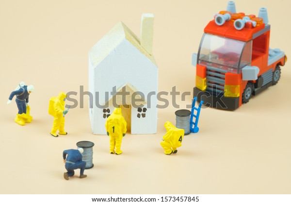 Miniature people figures of firefighters in hazard\
suits examining around\
home