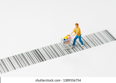 Miniature People Figurine With Grocery In The Shopping Cart Or Trolley Rally On The Bar Code Using As E-commerce With Copy Space, Consumer Or Buy And Sale In New Technology Channel Concept.