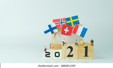 Miniature People Man And Woman Sitting On Wooden Block Number 2021 With National Country Flags On White Background With Copy Space