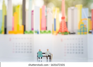 Miniature People: Old Couple Figure Sitting Long Chair On White Background With Copy Space Using As Background Business, Social Media Concept.