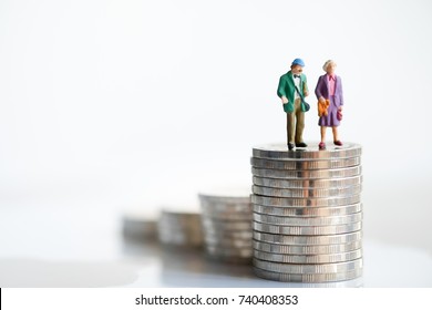 Miniature People: Old Couple Figure Standing On Top Of Stack Coins Using As Background Retirement Planning Concept.