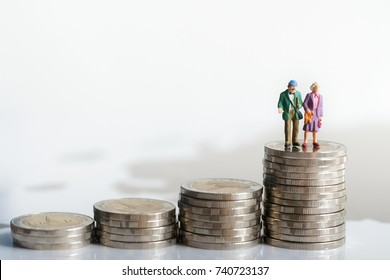 Miniature People: Old Couple Figure Standing On Top Of Stack Coins Using As Background Retirement Planning Concept.