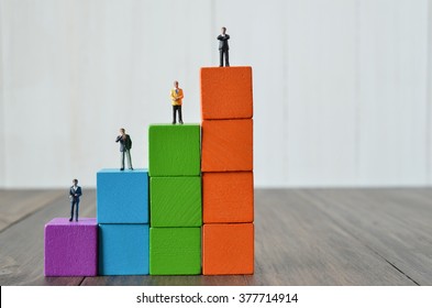 Miniature People On Stack Of Colorful Wooden Cube Building Blocks