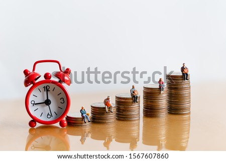 Miniature people: Red alarm clock and elderly people sitting on coins stack. Retirement planning. money saving and Investment. Time counting down for retirement and pension.