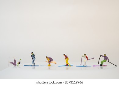 miniature people ride one behind the other on their skis. the first one lies on the ground because of a fall. Skier accident. white background, copy space. - Shutterstock ID 2073119966
