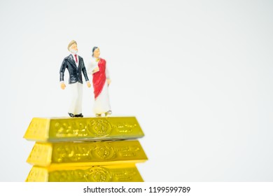 Miniature People :Senior Indian Couple And Rich People Stand On Pile Of Gold Bar  On White Background.Concept For Money, Financial, Business Planning,Gold Business And Rich People In India.