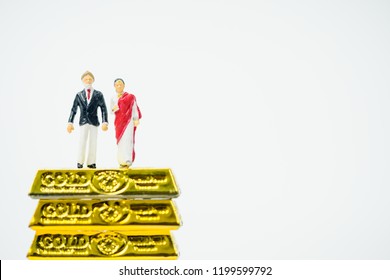 Miniature People :Senior Indian Couple And Rich People Stand On Pile Of Gold Bar  On White Background.Concept For Money, Financial, Business Planning,Gold Business And Rich People In India.