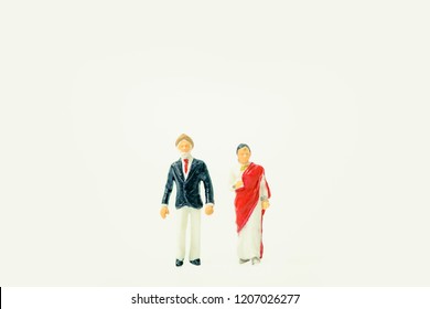 Miniature People :Senior Indian Couple And Rich People Stand On Pile Of Gold Bar  On White Background.Concept For Money, Financial, Business Planning,Gold Business And Rich People In India.