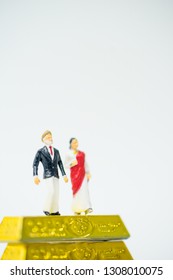 Miniature People :Senior Indian Couple And Rich People Stand On Pile Of Gold Bar On White Background.Concept For Money, Financial, Business Planning,Gold Business And Rich People In India.