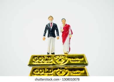 Miniature People :Senior Indian Couple And Rich People Stand On Pile Of Gold Bar On White Background.Concept For Money, Financial, Business Planning,Gold Business And Rich People In India.