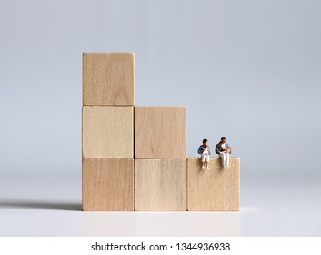 The Miniature People Sitting On A Block Of Stepped Wood. The Concept Of A Low Birth Rate.