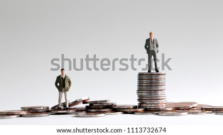 Miniature people standing on a pile of coins.