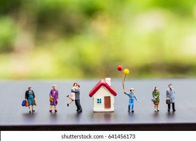 miniature people standing with tiny home on wooden floor over blurred spring green garden background.,Image for home sweet home concept.