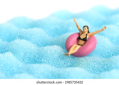Miniature people toy figure photography. Girl wearing black sunglass swimming with rubber tube ring on wavy ocean. Image photo