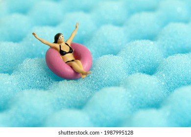 Miniature People Toy Figure Photography. Girl Wearing Black Sunglass Swimming With Rubber Tube Ring On Wavy Ocean. Image Photo