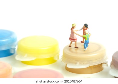 Miniature People Toy Figure Photography. Drawing Class Concept. A Group Of Kids Playing Above Paint Bottle, Isolated On White Background. Image Photo