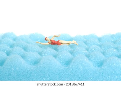 Miniature people toy figure photography. Swimming water sport. A young women freestyle swimmer above blue foam with wave pattern, isolated white background. Image photo