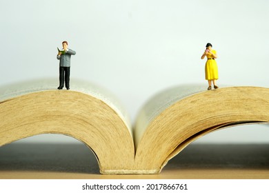 Miniature people toy figure photography. A men and girl couple stand reading on a opened book. Image photo - Powered by Shutterstock