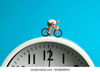 Miniature people toy figure photography. Cycling schedule concept. A biker cycling above clock, isolated on blue background. Image photo