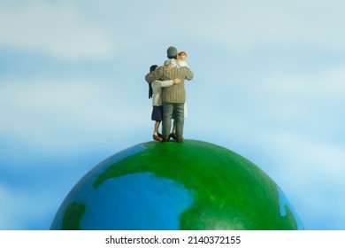 Miniature People Toy Figure Photography. Family Reunion Day Concept. Father Hugging His Wife And Daughter Above Earth Globe. Image Photo