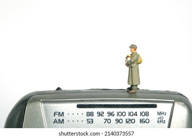 Miniature People Toy Figure Photography. A Military Mail Officer Holding News Pack Envelope Standing Above Radio Fm Device. Isolated On White Background. Image Photo