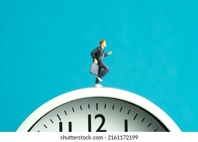 Miniature people toy figure photography. End and start of school concept. Young men pupil running above white clock isolated on blue background. Image photo