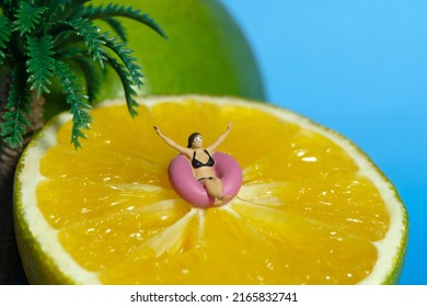 Miniature People Toy Figure Photography. Girl Wearing Black Sunglass Swimming With Rubber Tube Ring Above Slice Orange Fruit. Tropical Island With Palm Coconut Tree Concept. Image Photo