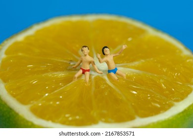 Miniature people toy figure photography. Two kids seat at the centre of sliced orange fruit. Isolated on blue background. Image photo
