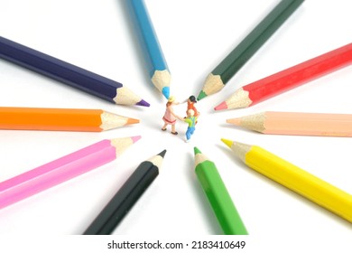 Miniature People Toy Figure Photography. Drawing Class Concept. A Group Of Kids Playing On Colorful Pencil, Isolated On White Background. Image Photo