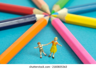 Miniature People Toy Figure Photography. Drawing Class Concept. A Group Of Kids Playing On Colorful Pencil, Isolated On Blue Background. Image Photo