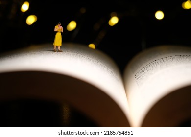 Miniature People Toy Figure Photography. A Girl Reading A Book At Night With Bokeh Defocused Light Lamp, Bed Time Routine Before Sleep. Image Photo