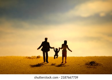 Miniature people toy figure photography. Couple with one child son daughter walking on sand beach at dawn. Family outing day concept. Image photo