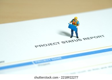 Miniature people toy figure photography. Project status report concept. A construction worker holding blueprint standing above progress report file on desk. Image photo - Shutterstock ID 2218922277