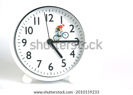 Miniature people toy figure photography. Cycling schedule concept. A biker cycling above clockwise, isolated on white background. Image photo