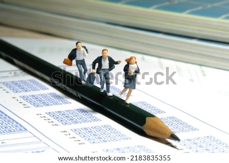 Miniature people toy figure photography. Late to attend examination day concept. Pupils running above pencil and exam answer paper sheet. Image photo