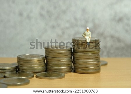 Miniature people toy figure photography. Income and salary growth. A men worker labor sitting above staircase coin pile. Image photo