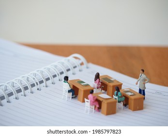 Miniature people toys on the paper book with blurred wooden table. Education and school concept.